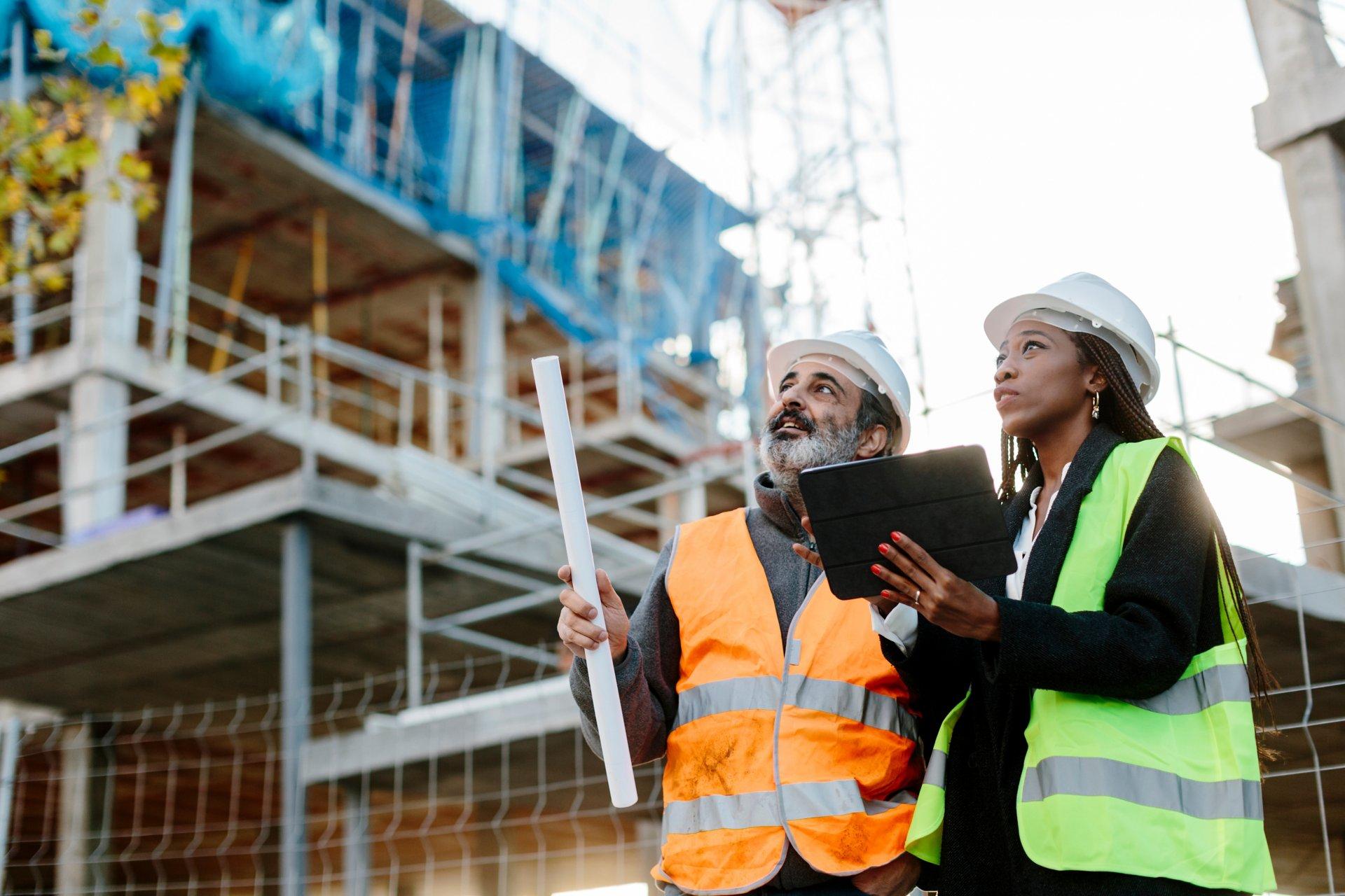 Woman engineer supervising construction of building with construction worker checking her tablet device