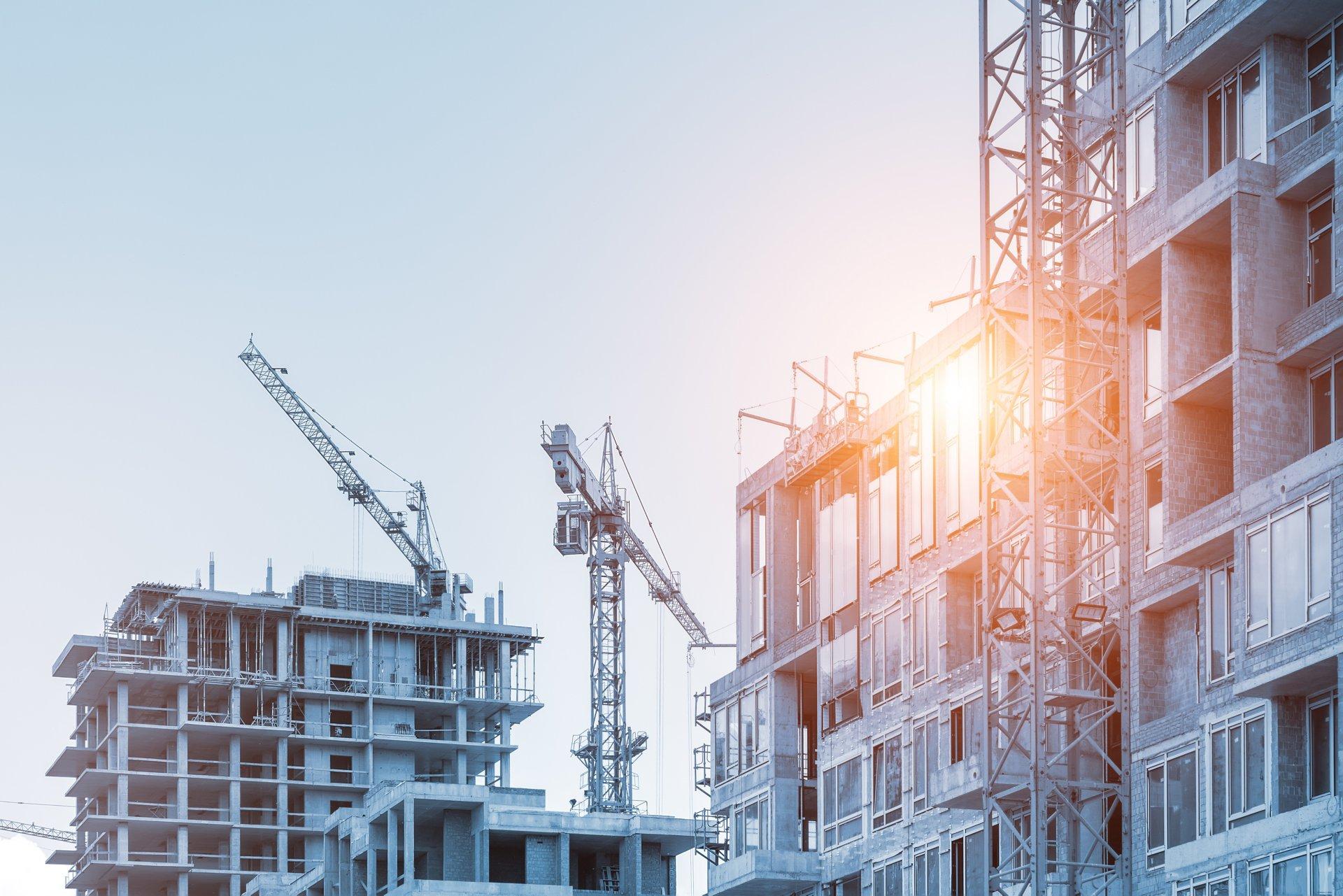 Modern apartment residential building glass facade wall construction site with many high tower cranes and heavy machinery against blue sky background. Industrial scenic urban city development project